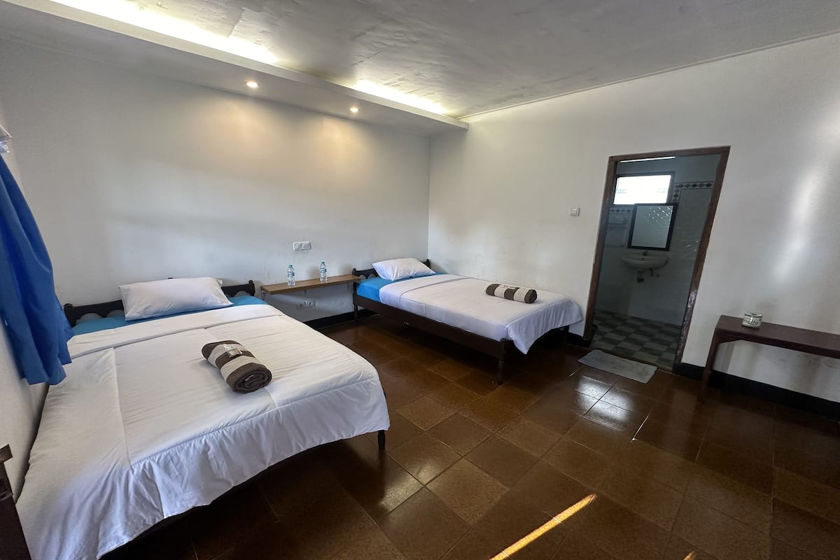 Ein Hotelzimmer mit zwei Einzelbetten, einem kleinen Tisch, einer Bank und einem Spiegel.