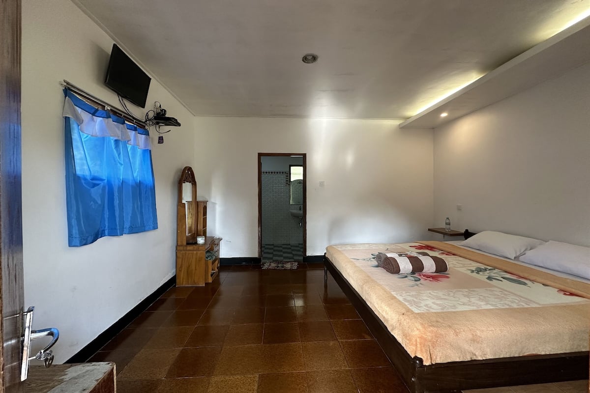 Ein Schlafzimmer mit einem Bett, einem an der Wand montierten Fernseher und einem durch eine offene Tür einsehbaren Badezimmer.