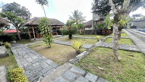 A courtyard with stone pathways, palm trees, and thatched-roof structures.