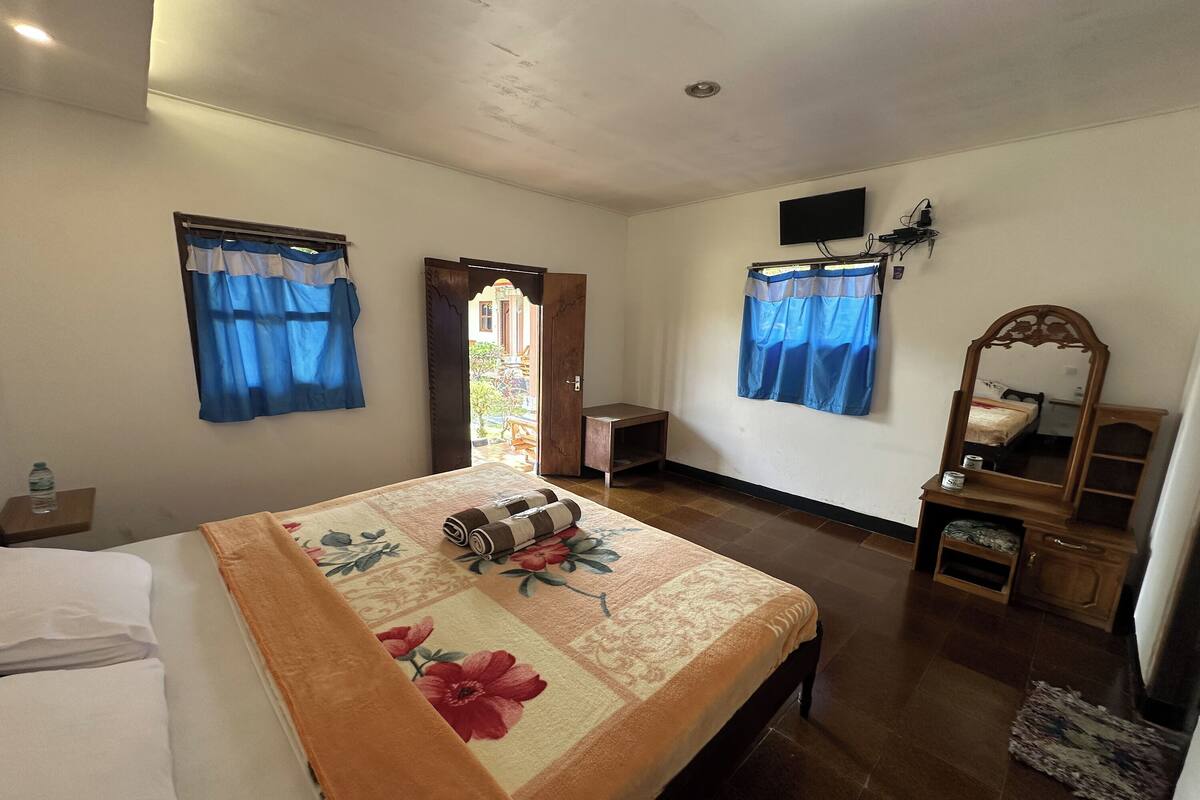 Ein Hotelzimmer mit einem Bett, einem Nachttisch aus Holz, einem Spiegel, einem kleinen Tisch und einer Tür, die auf einen Balkon führt.