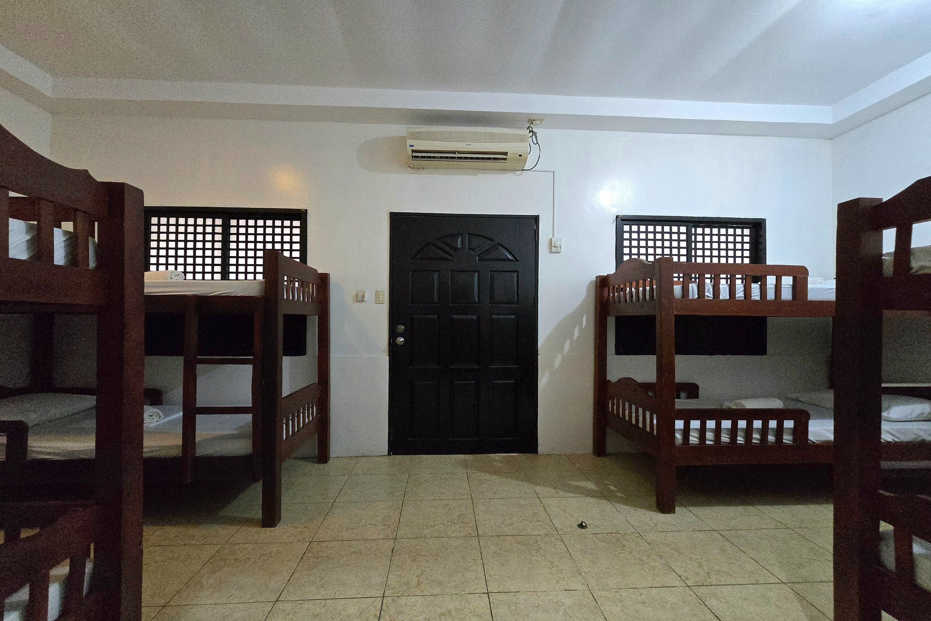 A room with bunk beds, a black door, and an air conditioning unit on the wall.