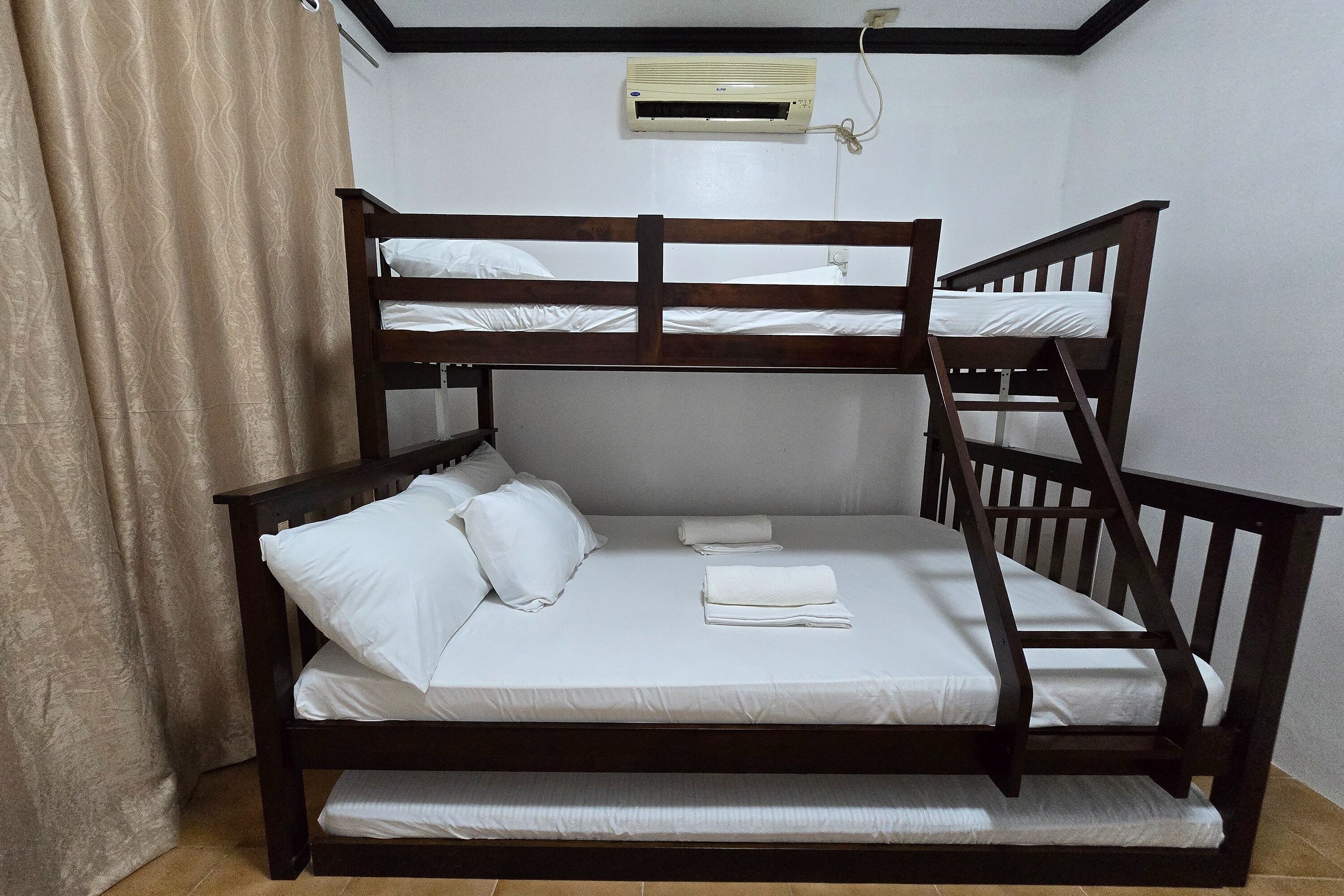 A bunk bed with white bedding and pillows, a wooden frame, and a ceiling-mounted air conditioning unit.