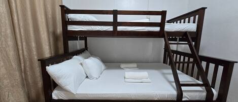 A bunk bed with white bedding and pillows, a wooden frame, and a ceiling-mounted air conditioning unit.
