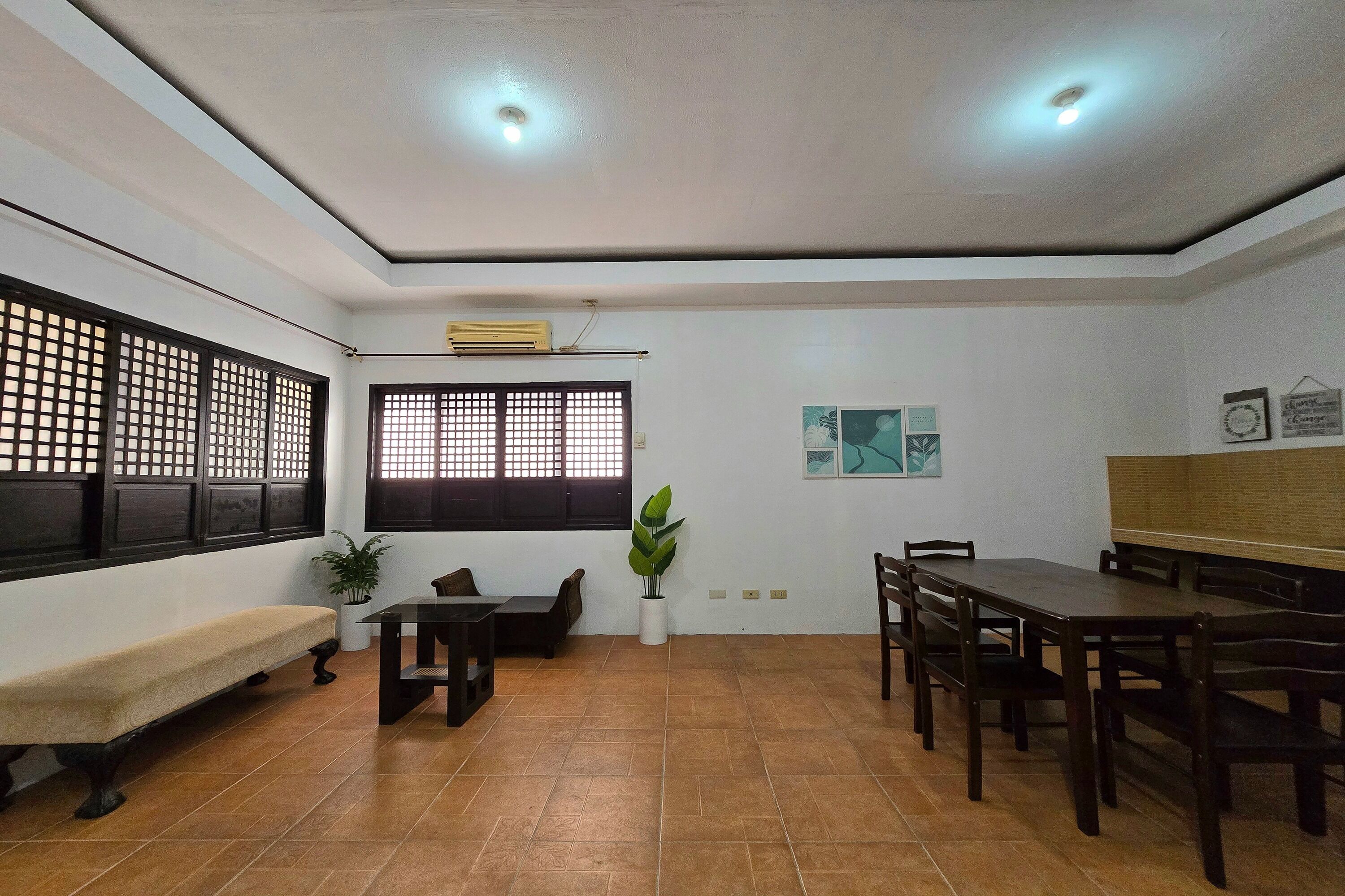A dining area with a bench, wooden tables, chairs, a potted plant, and a window with a grid pattern.