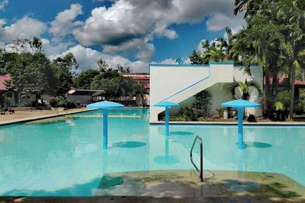 A swimming pool with blue umbrellas, surrounded by palm trees and a clear sky. - Grand Villa Laguna (Bay)