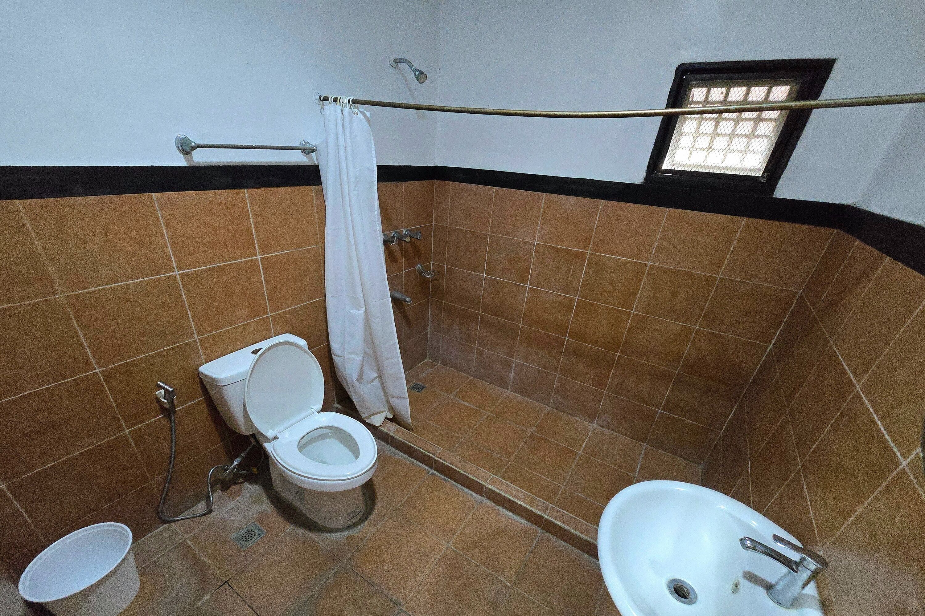 Un baño con inodoro, lavamanos, ducha y una ventana pequeña.
