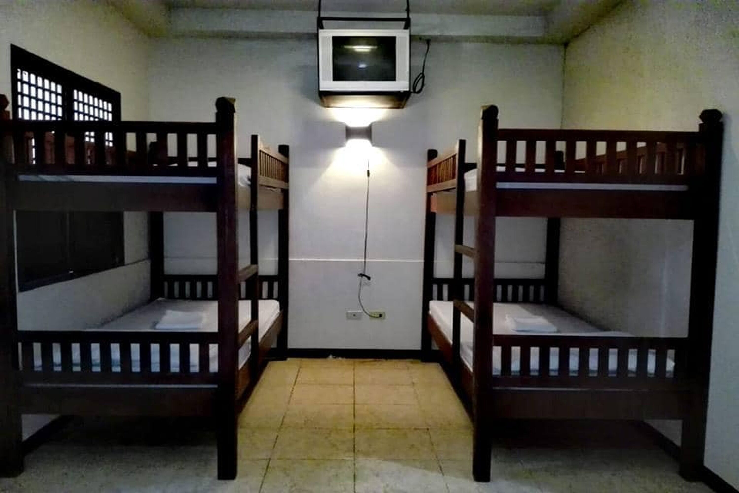 A room with two bunk beds, a television mounted on the wall, and a light fixture above the beds.