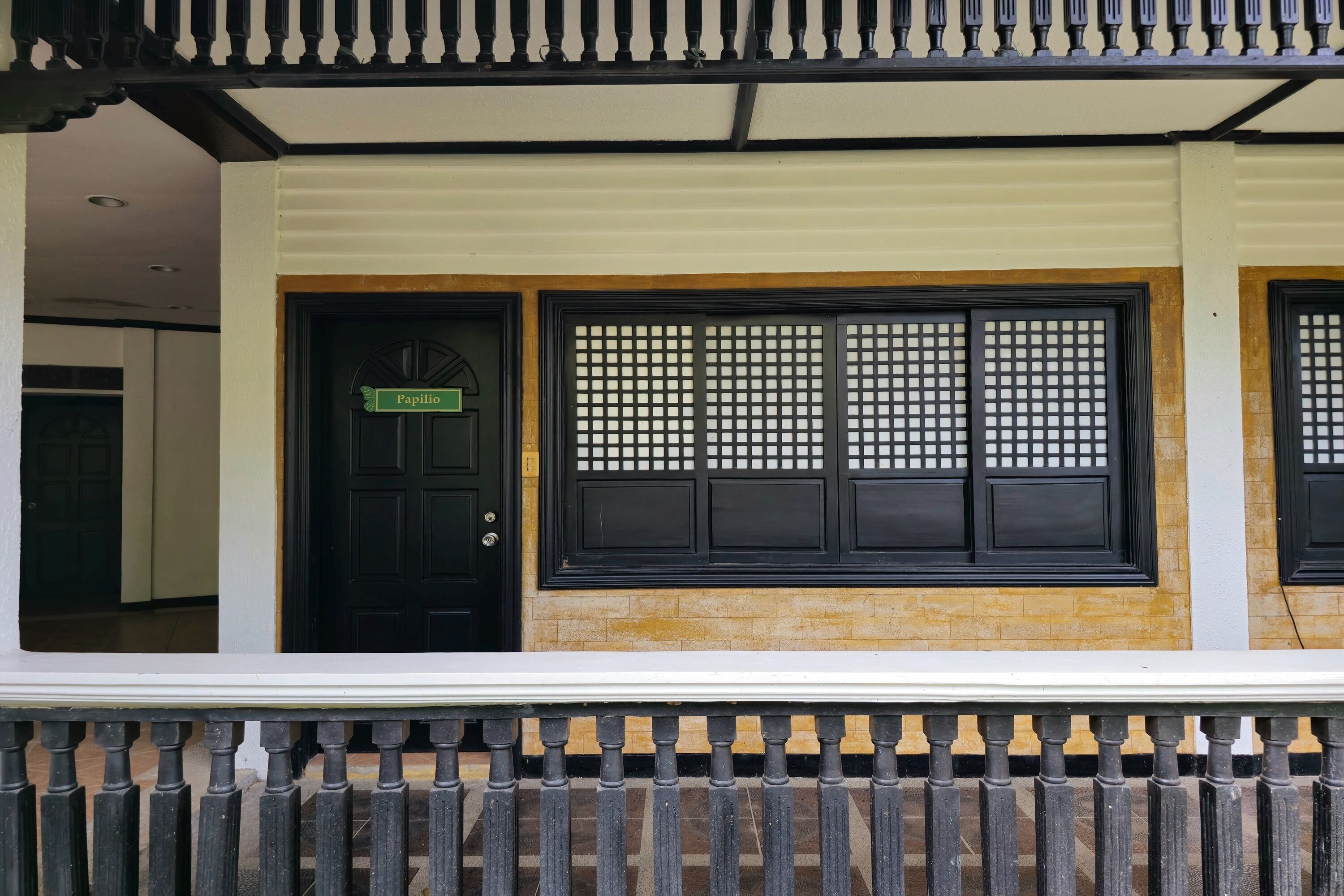 A traditional building with a black door, a window with a grid pattern, and a white railing.