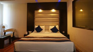 A hotel room with a large bed, a bedside table, a chair, and a desk. - Hotel Billions (Gurugram)