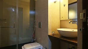 A bathroom with a glass shower enclosure, a toilet, and a sink with a mirror above it. - Hotel Billions (Gurugram)