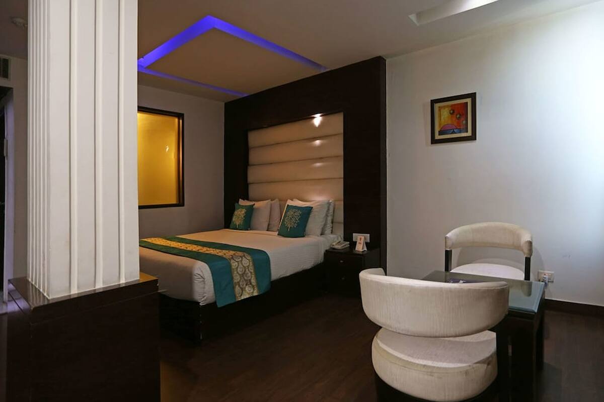 A modern hotel room with a bed, bedside table, chair, and a painting on the wall.