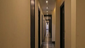 A long, narrow hotel corridor with doors on both sides, recessed lighting on the ceiling, and a shiny floor. - Hotel Billions (Gurugram)
