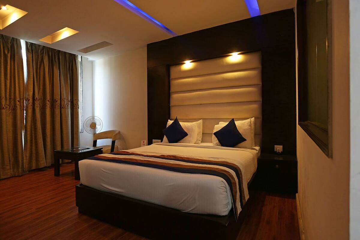 A modern hotel room with a large bed, a bedside table, a chair, and a large window with curtains.