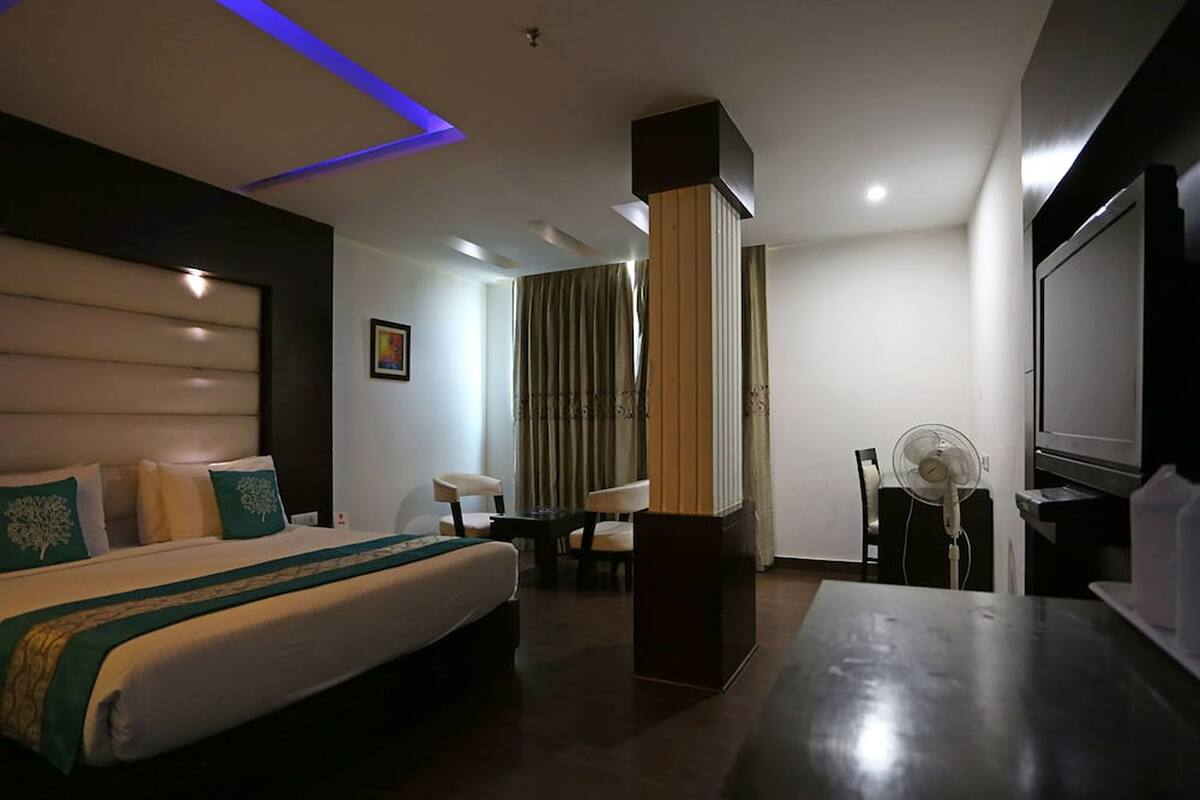 A hotel room with a bed, a desk, a chair, a TV, and a fan.