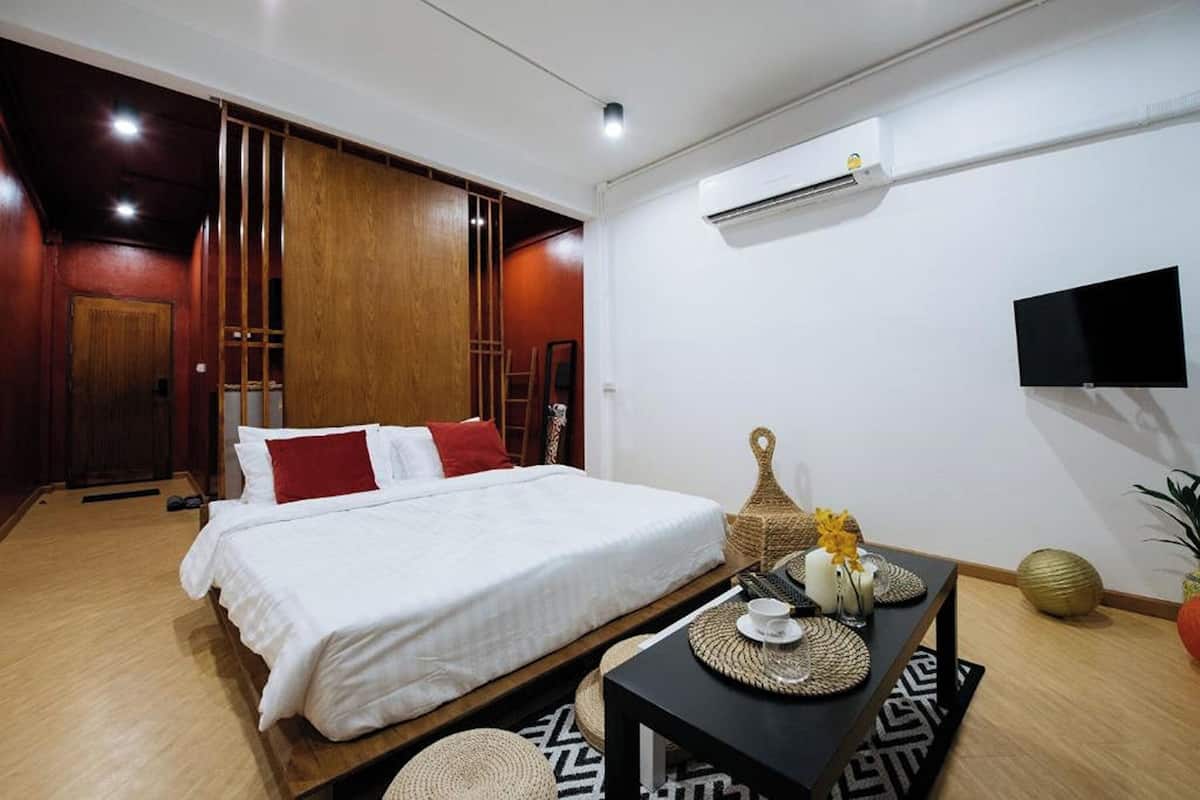 A hotel room with a bed, a small table with a vase and a candle, a wall-mounted TV, and an air conditioning unit.