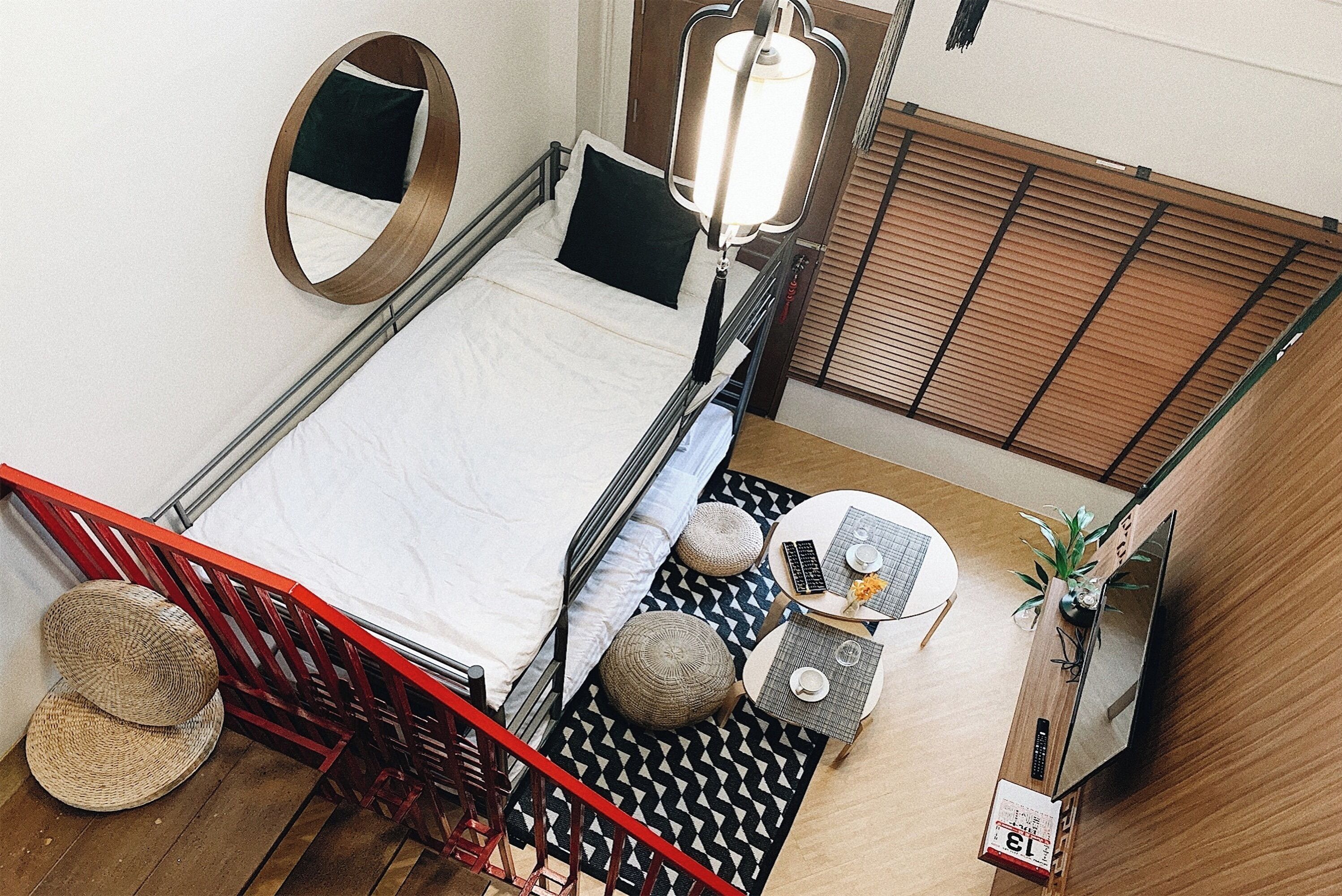 Un dormitorio con cama, mesita de noche, lámpara y un espejo redondo pequeño.