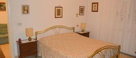 A bedroom with a bed, two bedside tables, a nightstand, and a wall-mounted air conditioner.