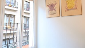 A room with a large window overlooking a balcony with railings and potted plants. There are two framed artworks on the wall.