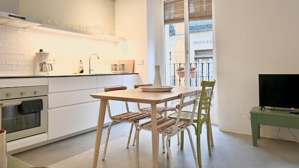 A modern kitchen with white cabinetry, a coffee machine, and a dining area with a wooden table and chairs.