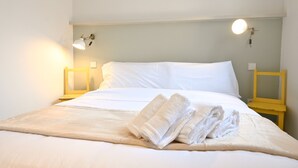A neatly made bed with white linens and towels, two bedside tables with lamps, and a light switch on the wall.