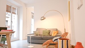 A modern living room with a grey sofa, a small side table, a wicker chair, and a floor lamp.