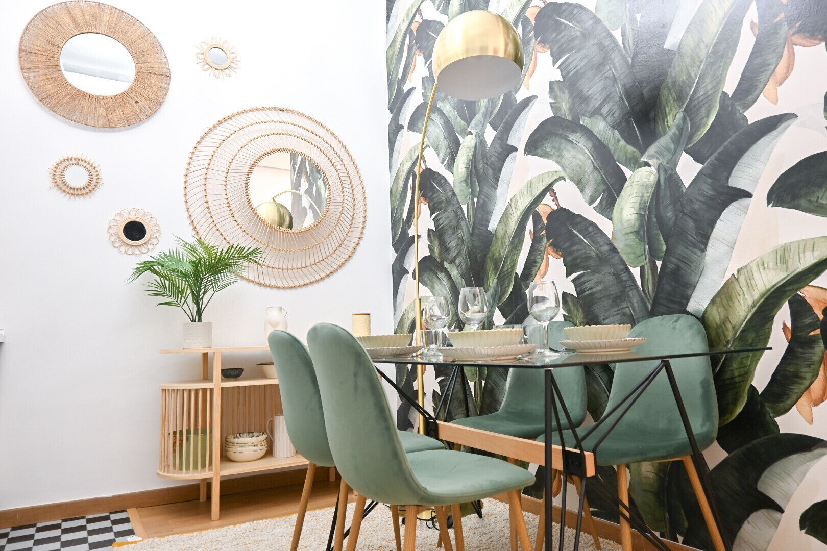 A dining area with a round table, green chairs, and a wall with a large plant mural.