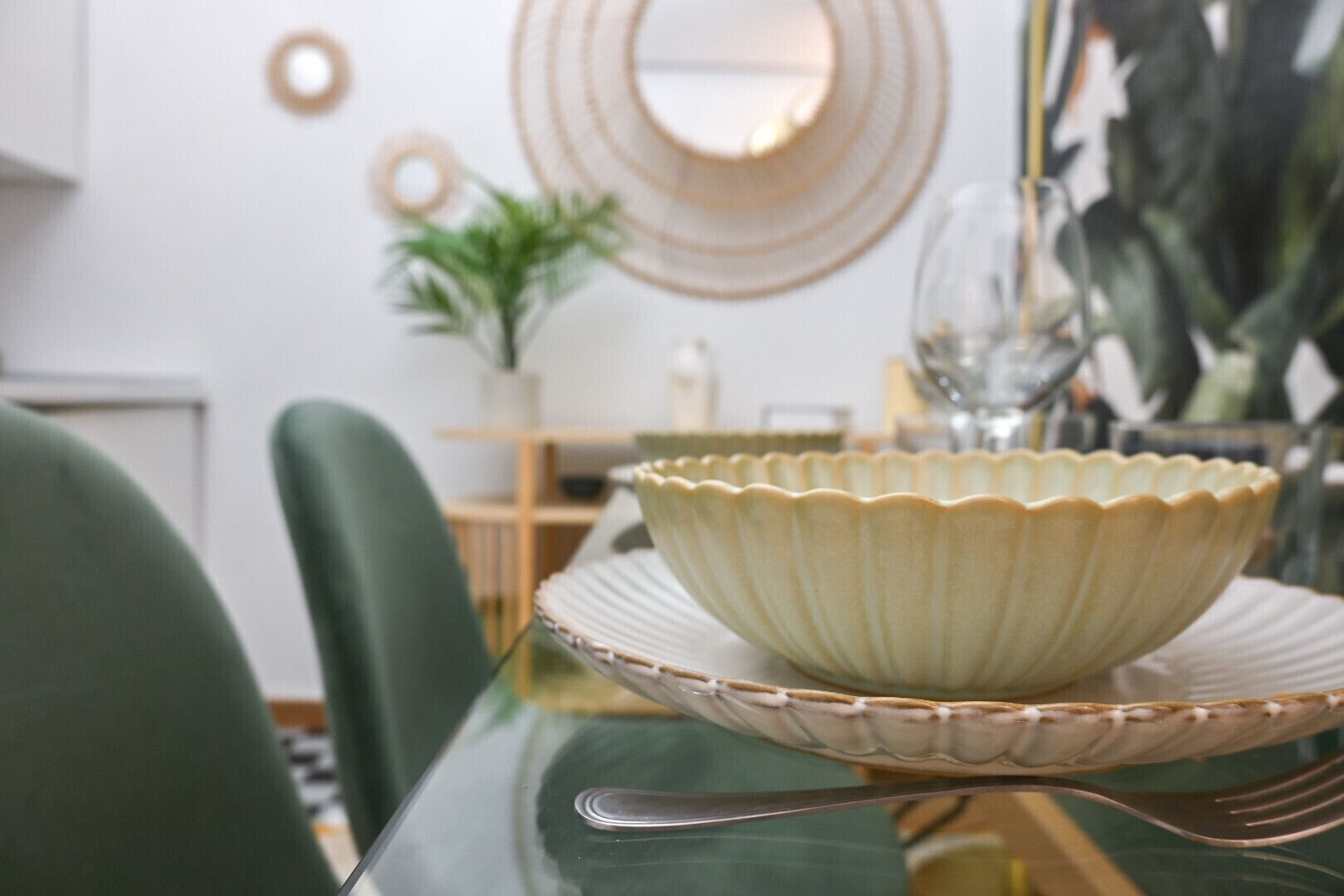 A dining table with a decorative bowl, a green chair, and a mirror on the wall.