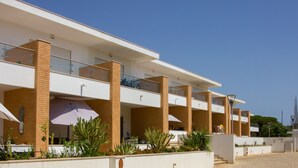 Ein modernes Hotel mit mehreren Balkonen, einer überdachten Außenbereich-Sitzgelegenheit und einem angelegten Garten.