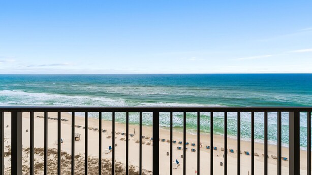 A beach view from a balcony with a railing, featuring a sandy beach with rows of beach chairs and umbrellas, and the ocean in the background. - New Renovation, Gulf Front, Commodore 25+ (Panama City Beach)