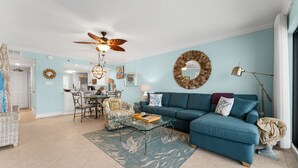 A living room with a blue sofa, a glass coffee table, and a ceiling fan. - New Renovation, Gulf Front, Commodore 25+ (Panama City Beach)