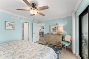 A bedroom with a bed, a ceiling fan, a dresser, a chair, and a window.