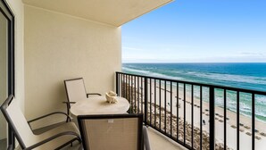A balcony with a table and chairs, overlooking a beach with people and beach chairs. - New Renovation, Gulf Front, Commodore 25+ (Panama City Beach)