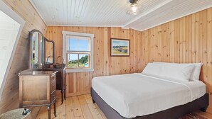 Ein Schlafzimmer mit holzgetäfelter Wand, einem Bett mit weißer Bettwäsche, einem Fenster mit Aussicht und einem Schminktisch mit Spiegel.