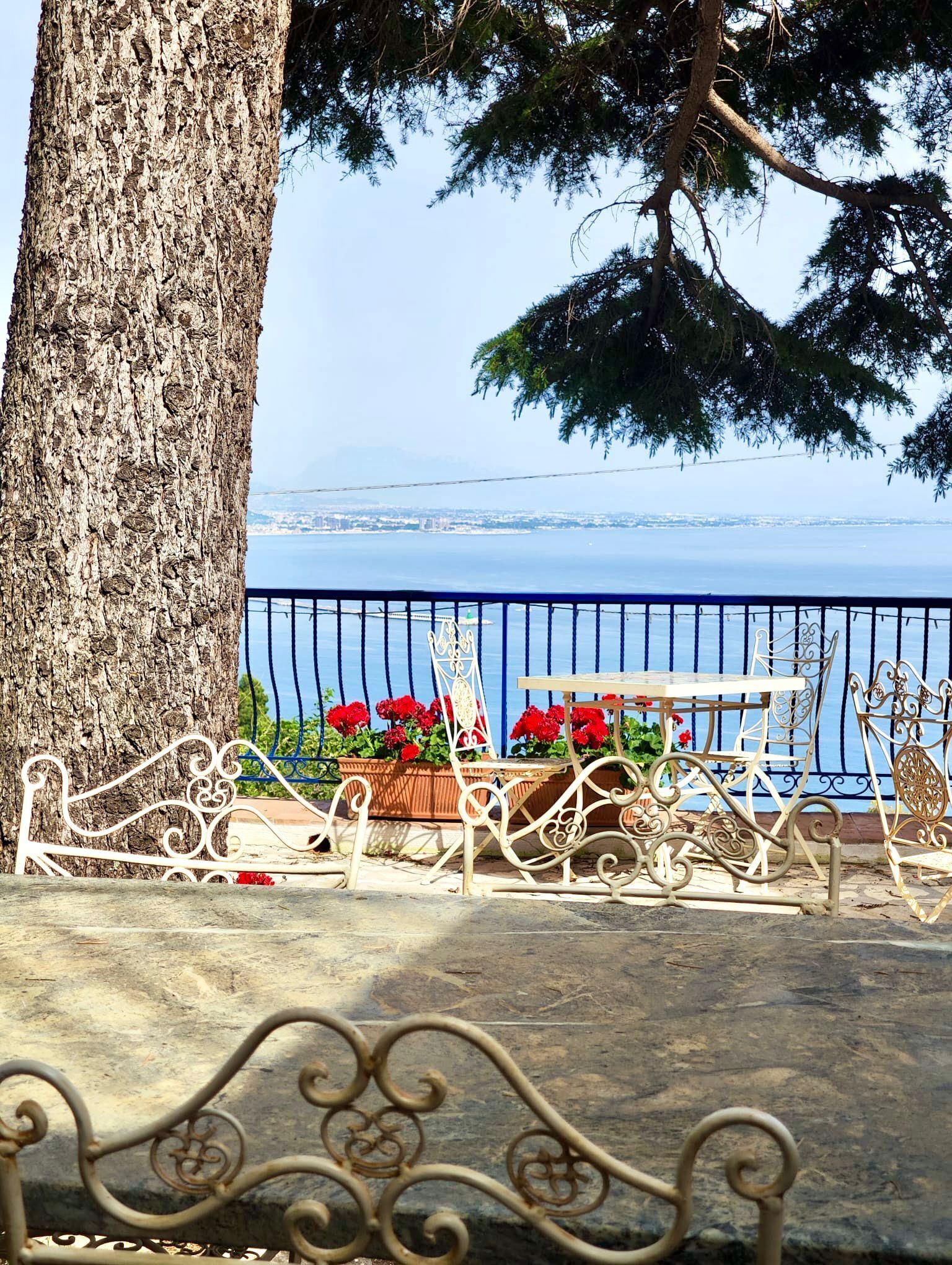 Un banco con barandillas metálicas, un árbol y vista al mar.