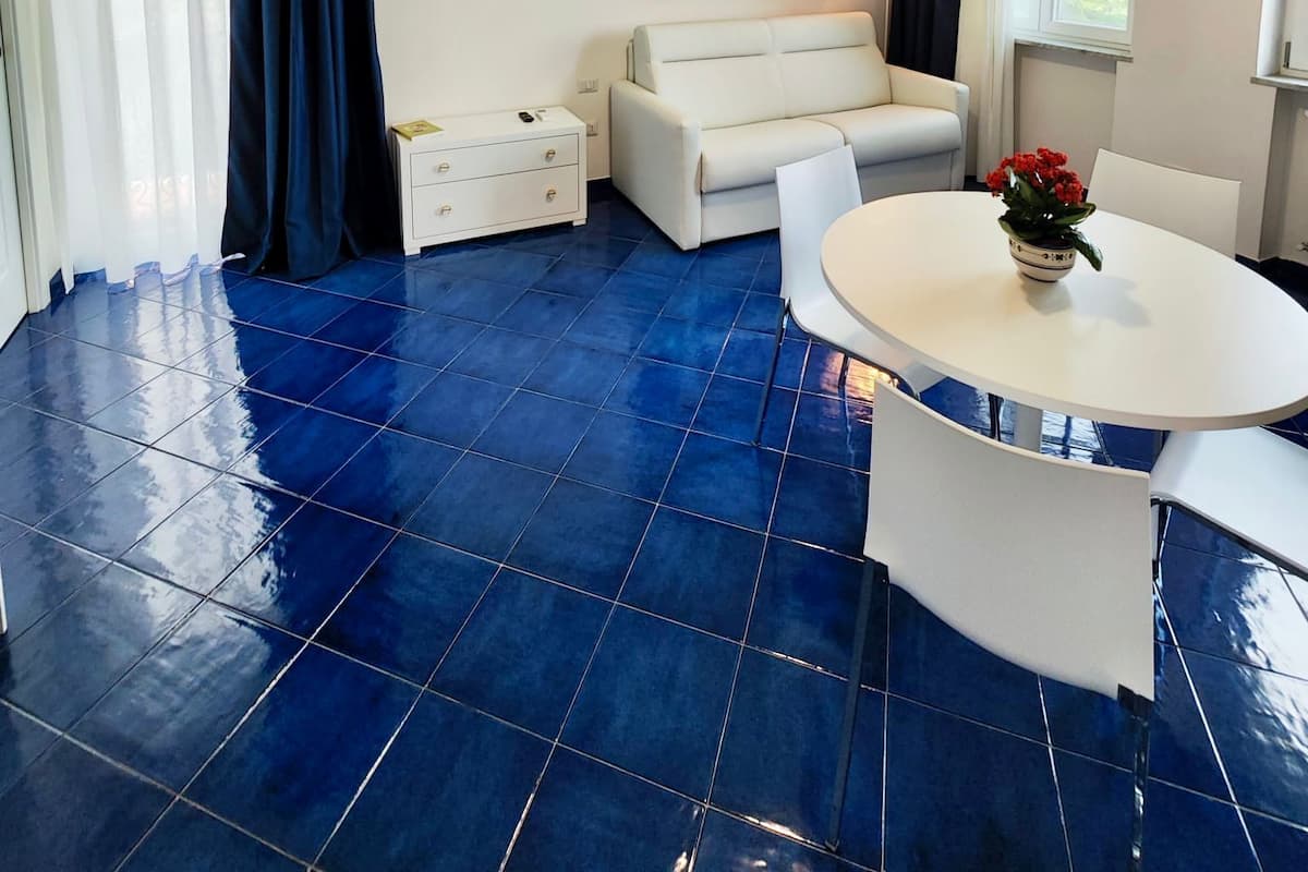 A modern living room with a blue-tiled floor, white furniture, a painting on the wall, and a ceiling fan.