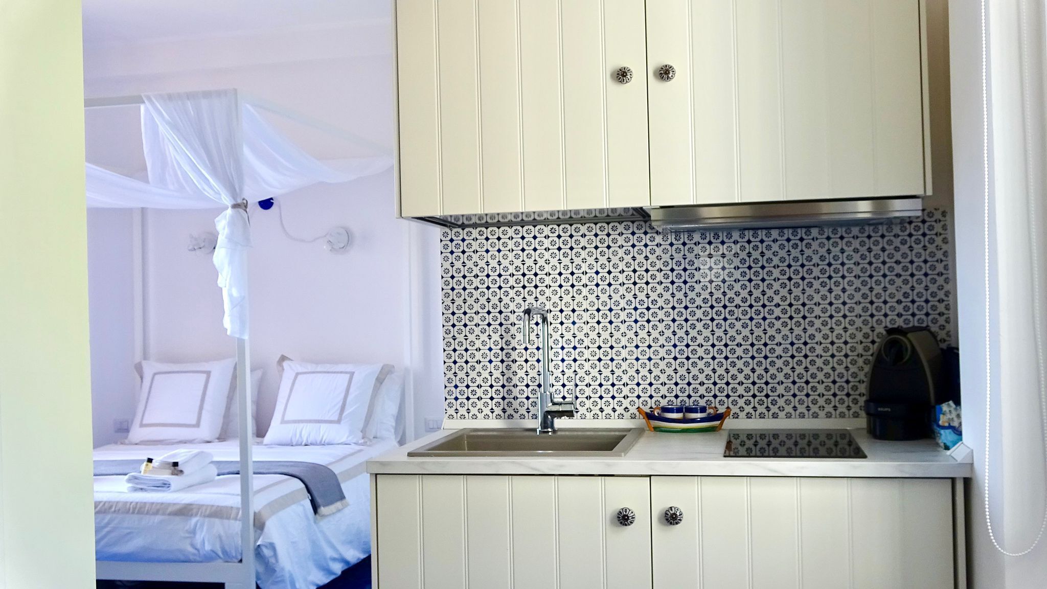 A compact hotel room with a bed, a small kitchenette, and a bathroom with a shower curtain.