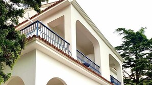 Un edificio de dos pisos con fachada blanca, contraventanas azules y un balcón con barandilla de metal.