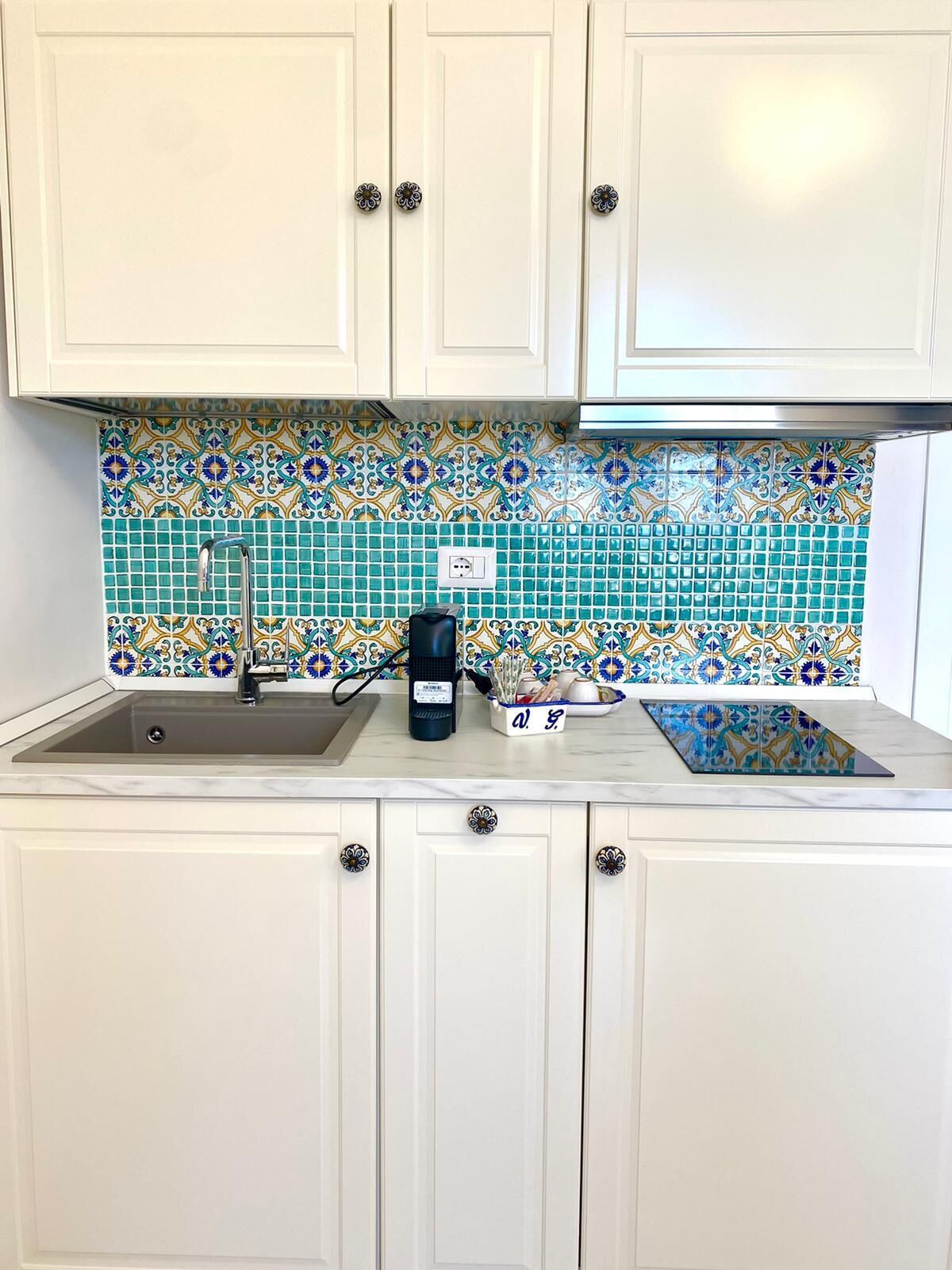 A kitchen with white cabinets, a sink, a coffee maker, and a patterned backsplash.