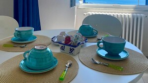 Una mesa redonda con tazas y platillos azules, una tetera y una bandeja con tazas y una cuchara.