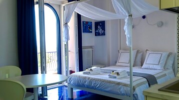 Habitación de hotel con cama, una mesa y una silla. Se ve una ventana con cortinas y una obra de arte en la pared.