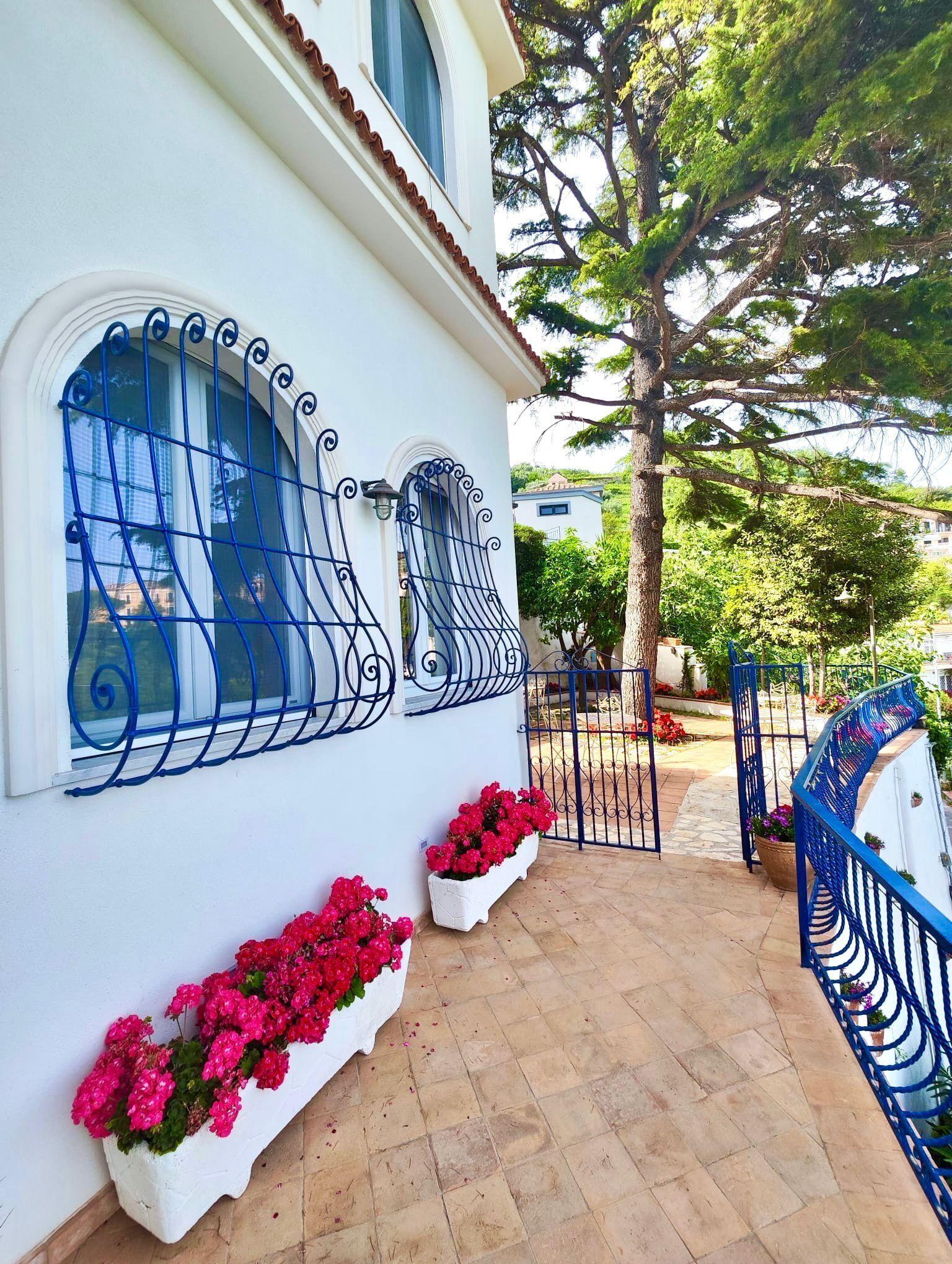 A building with a white facade, blue window railings, and a tiled patio area with flower planters.