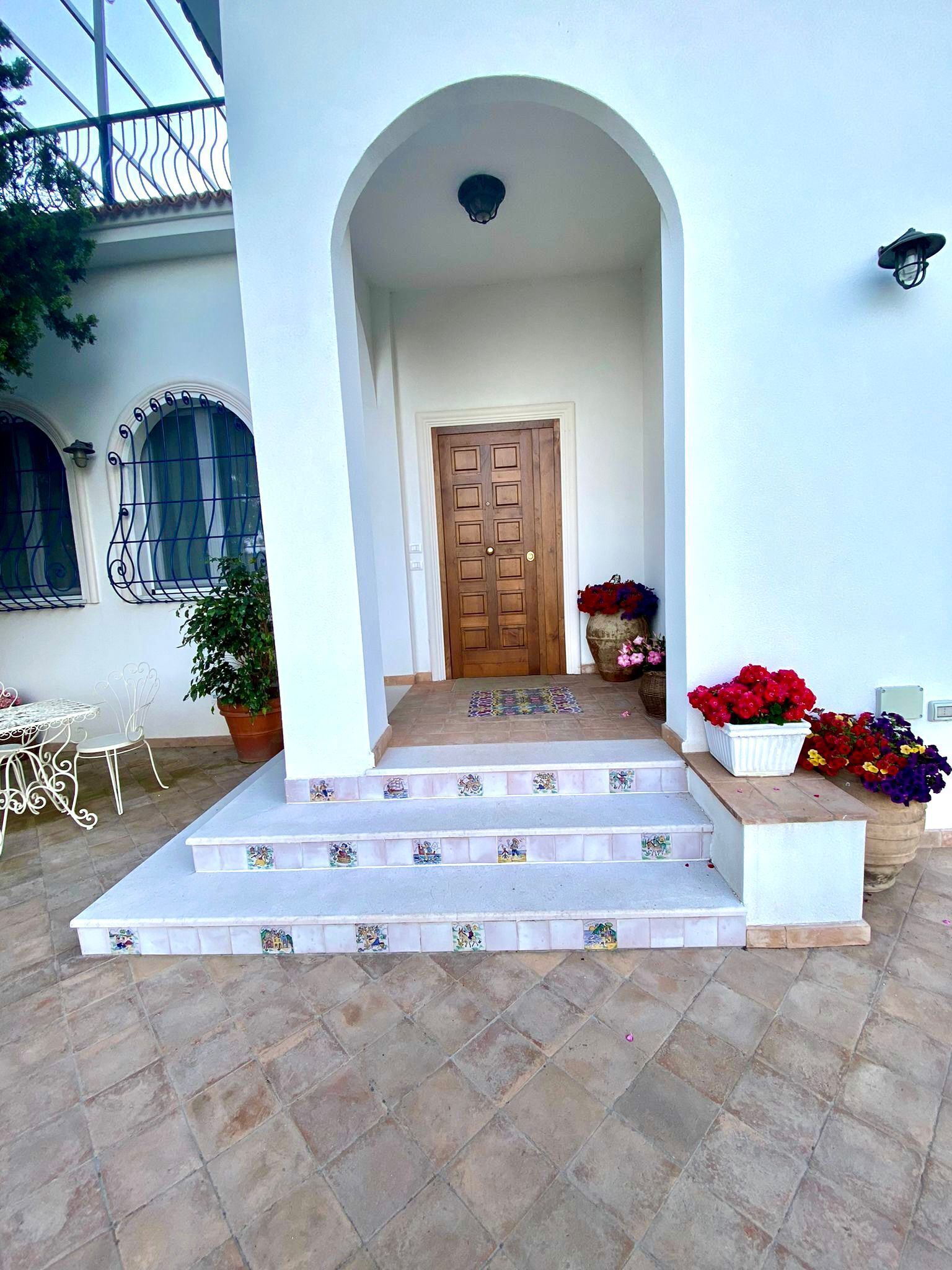 A white building with a wooden door, a tiled entrance, and potted plants.