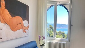 Una sala de estar moderna con un sofá azul, un cuadro en la pared, vista al mar a través de un ventanal grande y un radiador blanco.