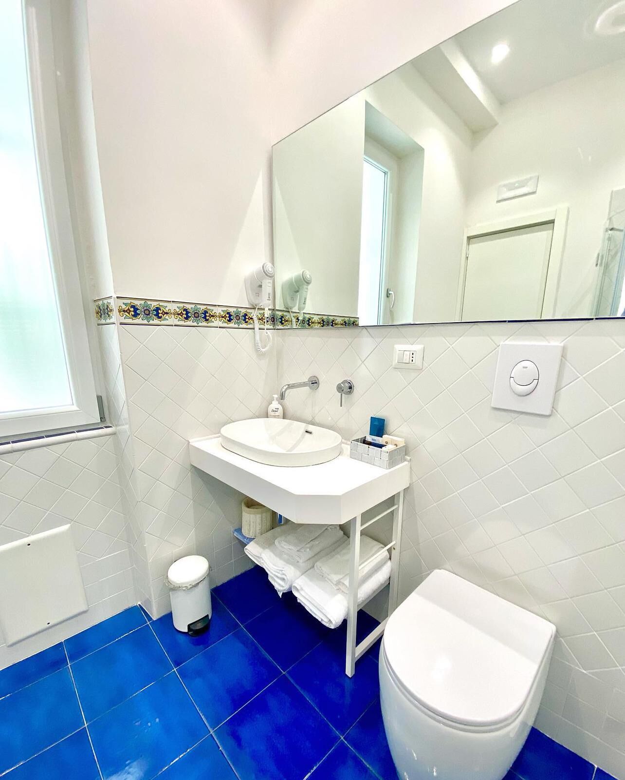 Un baño con lavamanos blanco, un espejo, inodoro y suelo con azulejos azules.
