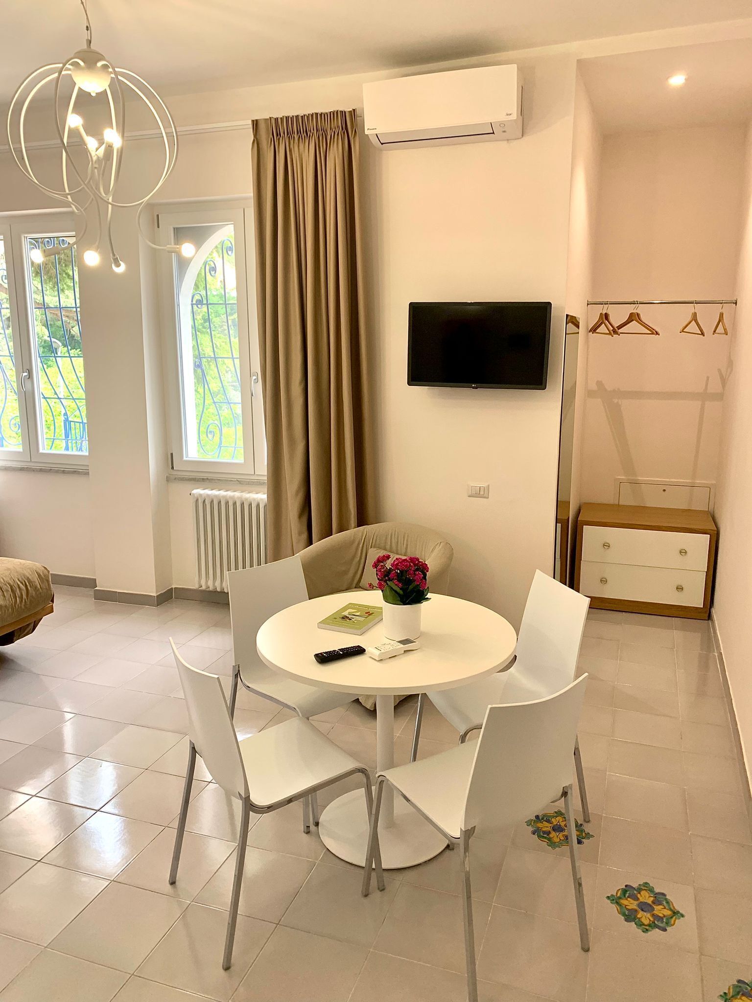 A modern living room with a round dining table, white chairs, a flat-screen TV, and a window with curtains.