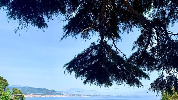 Un balcón con mesa y sillas que ofrece vistas al mar, con barcos y vegetación.