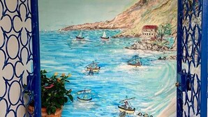 Un mural que muestra una escena costera con barcos y un edificio sobre un acantilado.
