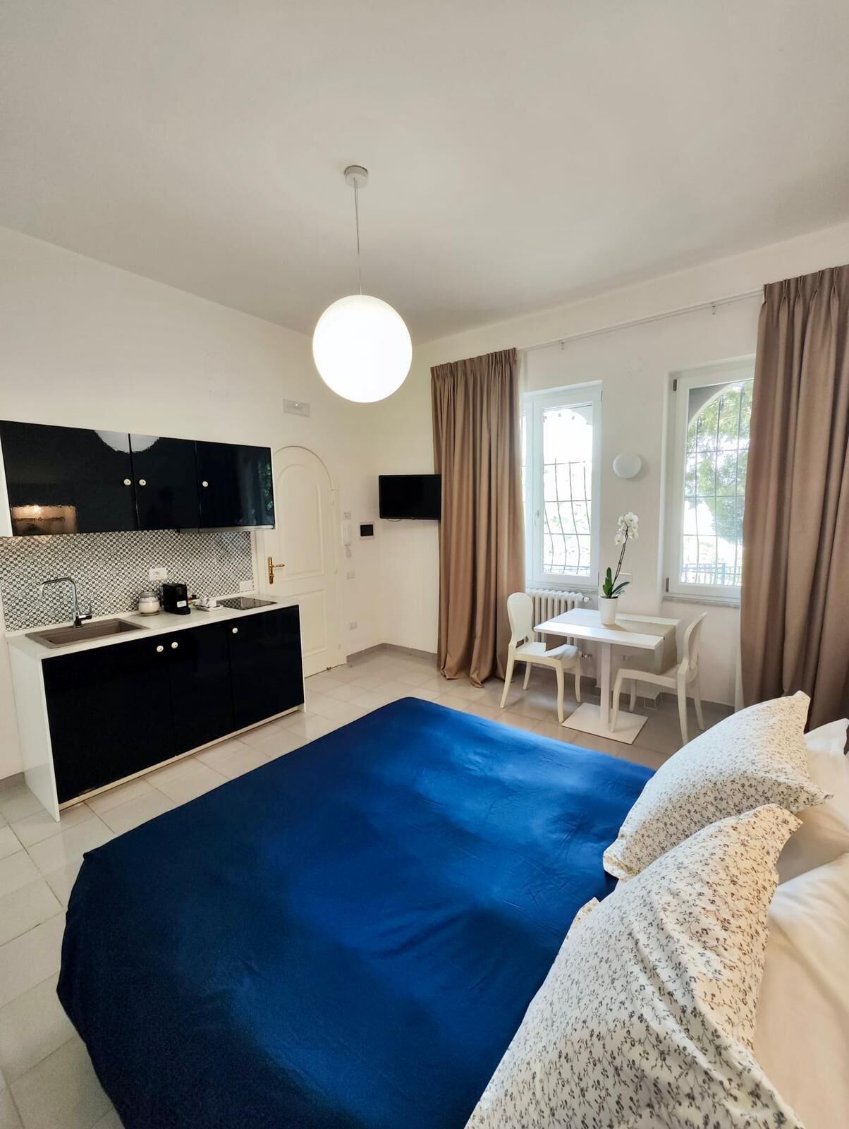 A modern bedroom with a large bed, a small kitchenette, and a dining area.