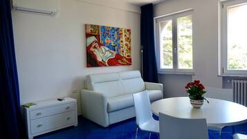 A modern living room with a white sofa, a dining table with a vase of flowers, and a large painting on the wall.