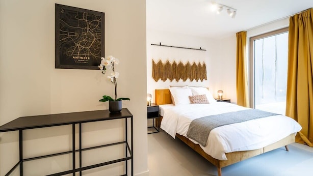 A modern hotel room with a large bed, a map on the wall, a bedside table with a lamp, and a window with curtains.